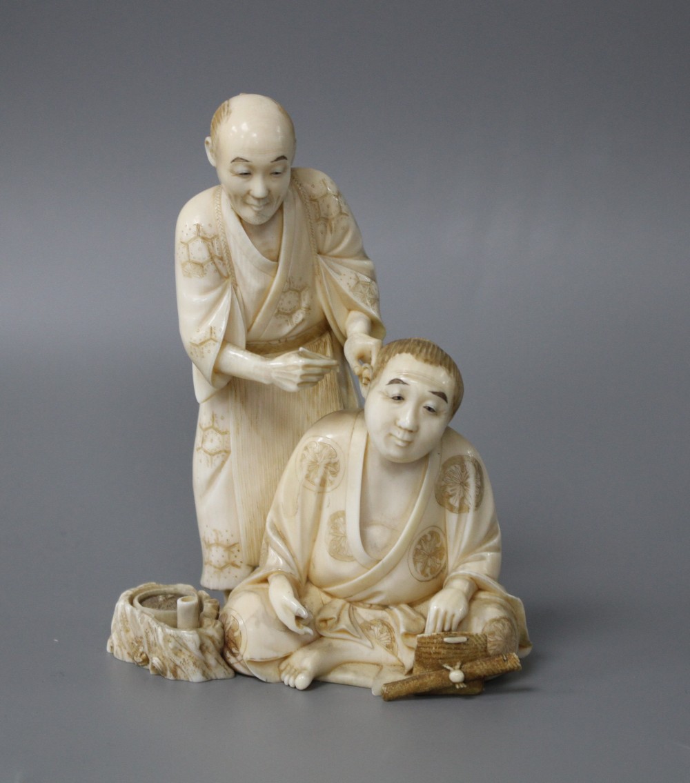 A Japanese Meiji period ivory okimono carved with a doctor treating a mans ear, signed, height 12cm
